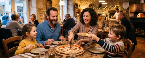 Une famille partage une grande pizza artisanale autour d'une table en bois dans une pizzeria au décor rustique français